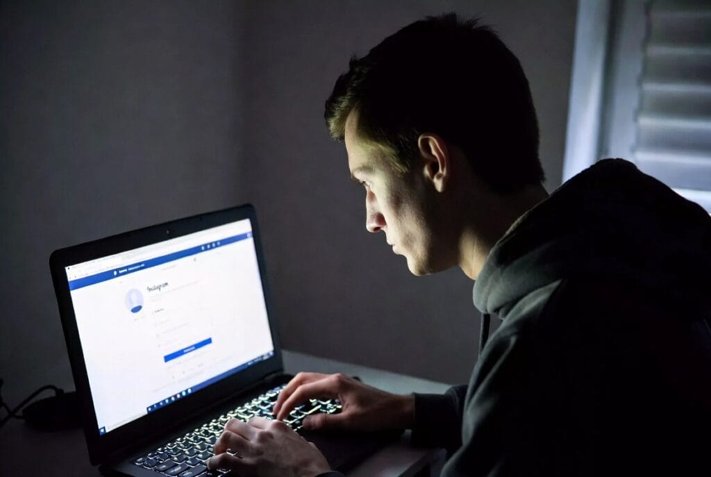 A person viewing a smartphone screen showing an Instagram direct message log and a separate private monitoring dashboard on a laptop